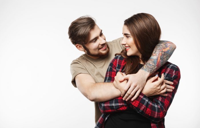 Nice man hugging woman from behind. Looking at each other with smile. Looking glad.