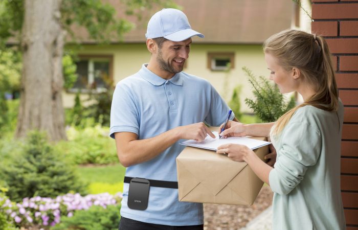 Young courier holding a parcel, woman signing a delivery form